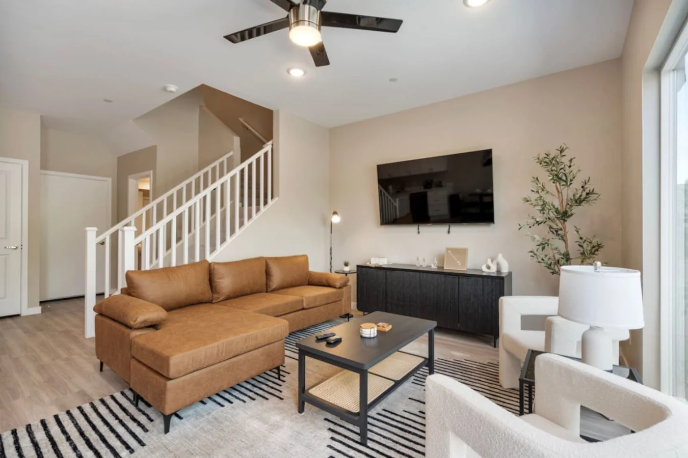 The living room is filled with natural light, creating a bright and welcoming space that invites relaxation. It features a comfy sofa and a 65-inch UHD Smart TV for your entertainment.