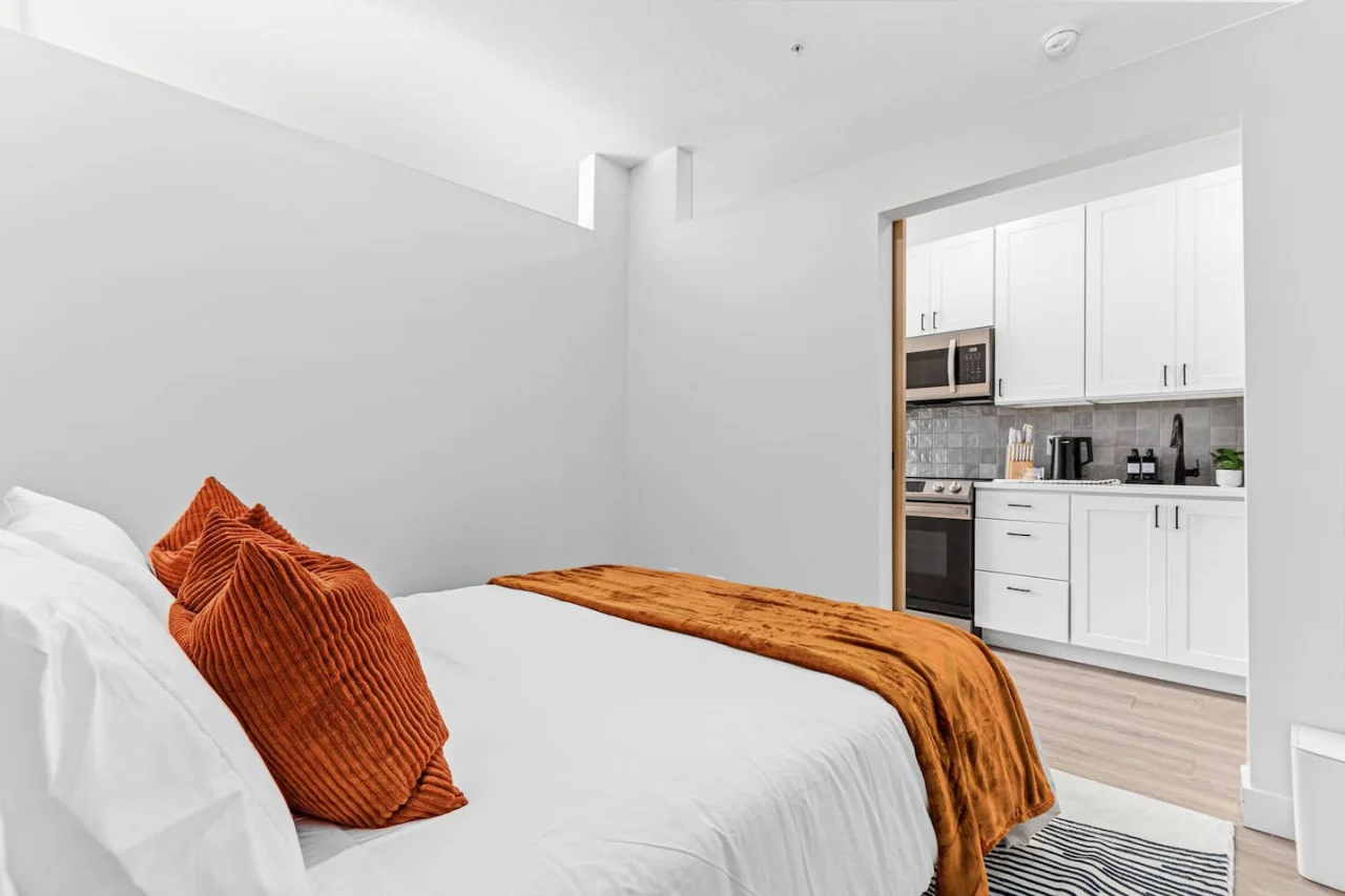 Comfortable Queen size bed - Area rug - Extra pillows w/ Throw blanket - Sliding bedroom door - View of the kitchen through the open bedroom door