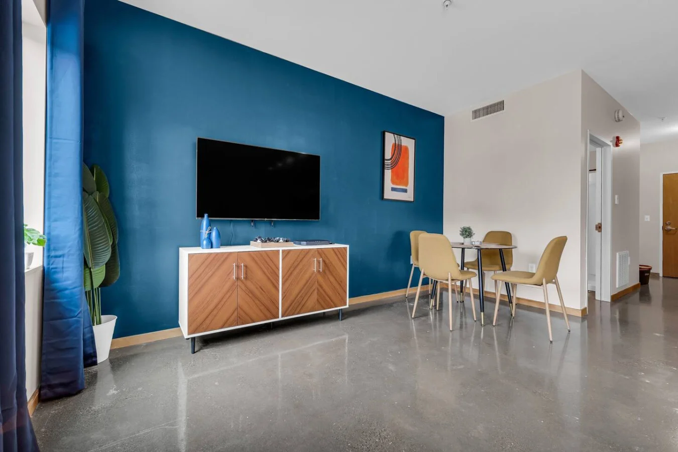 Spacious open-concept living and dining area featuring a vibrant blue sofa, modern furnishings, and a stylish entertainment setup—ideal for gatherings and relaxation.