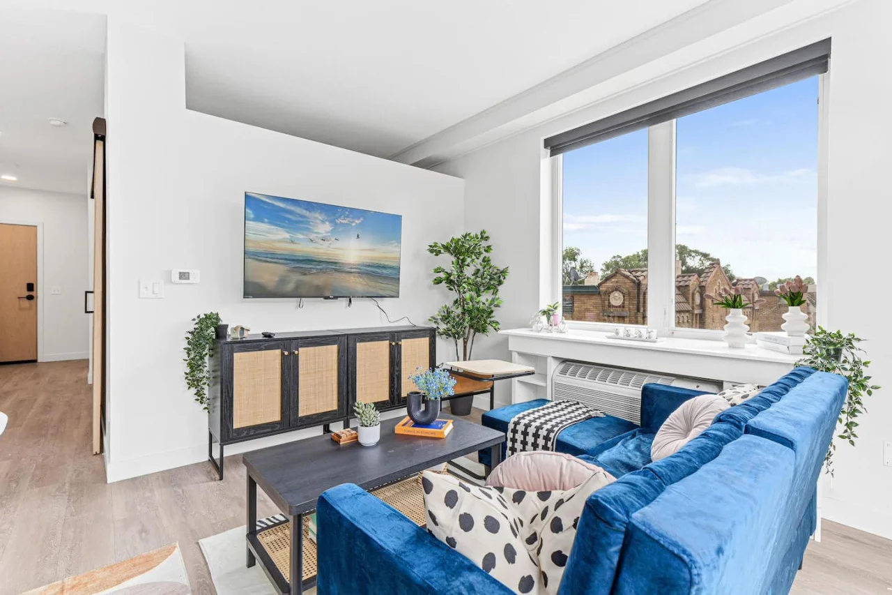 Cozy Couch with Throw pillows - Coffee table - Area rug - 55" Smart TV - Large windows w/ Natural light - Room darkening shades - Side table & Plants - View of Historic building.
