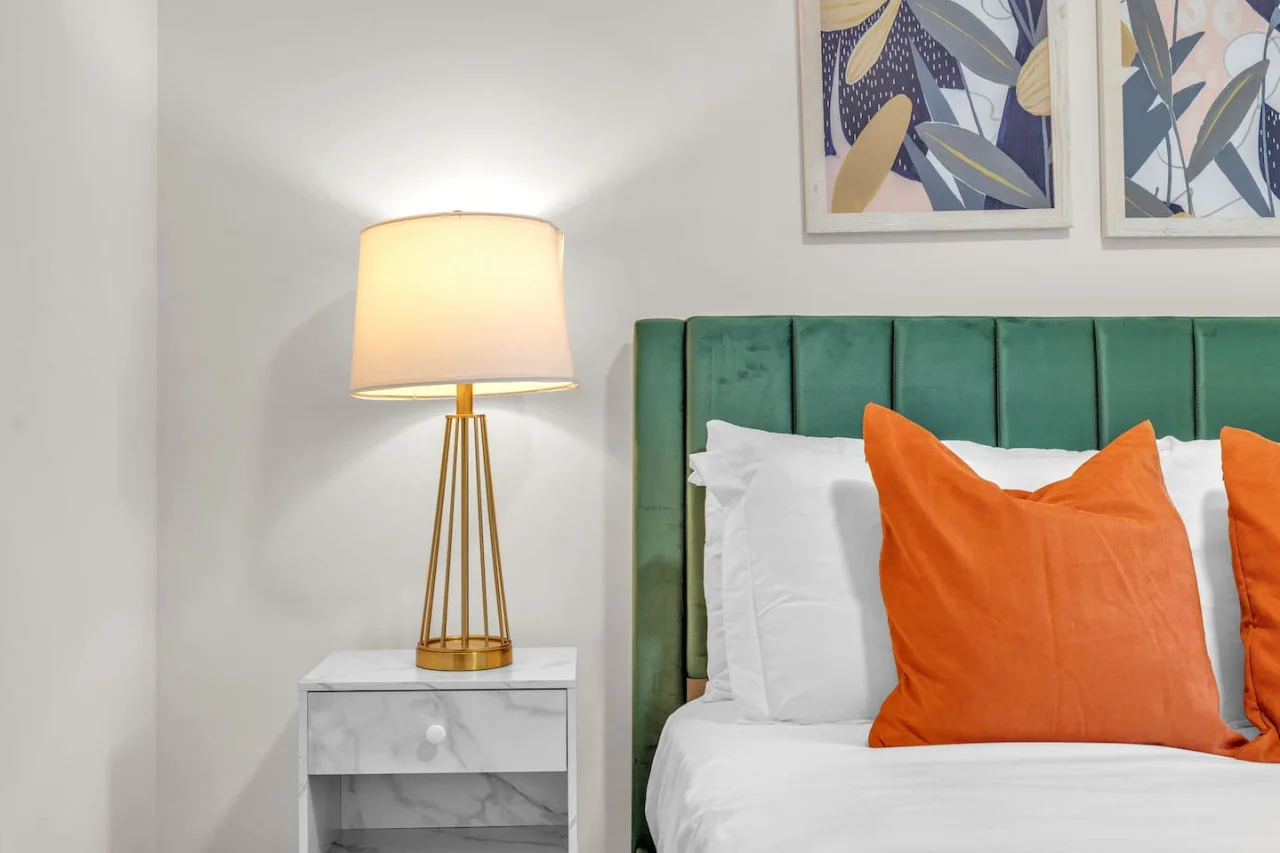 A cozy and stylish bedroom with a green upholstered bed frame, warm lighting, and abstract wall art for a contemporary vibe.