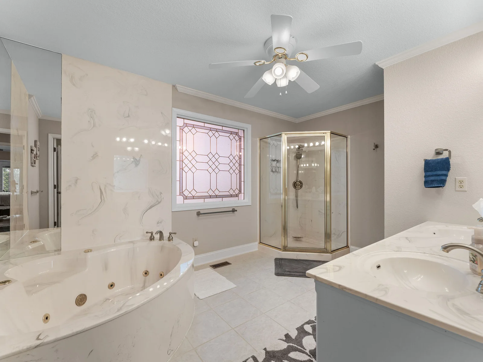 Soaking tub for two with brass fixtures, a glass-enclosed walk-in shower with marble tile, and a leaded art-glass window that fills the room with light. The primary bath earns it.