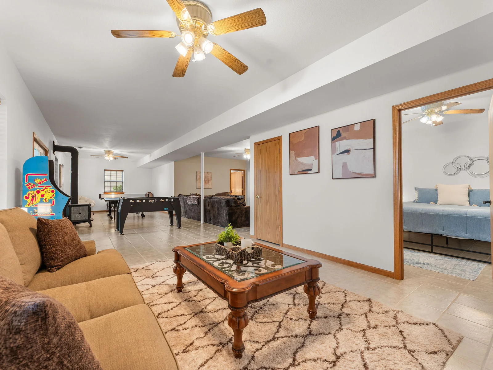 A wide view of the entire basement level: rec room, lounge, game tables, and the hallway to the bedrooms all in one frame. This is the floor the kids never want to leave.