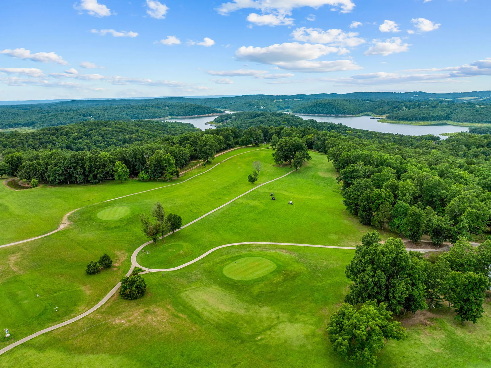 The golf facilities at Lost Woods Hideaway from the air — driving range, practice greens, and Bull Shoals Lake framing the whole picture. Golf and lake in one trip.