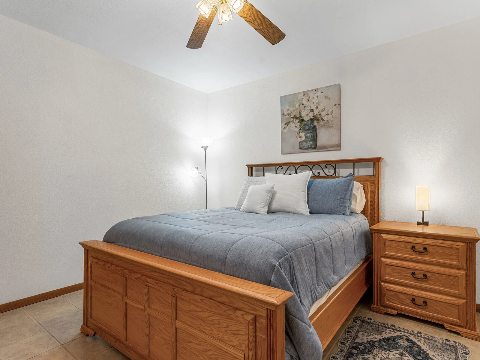 A quiet queen bedroom in the basement, with tile floors, a sliding barn door, and warm bedside lighting. Sleeps one couple away from the noise of the floors above