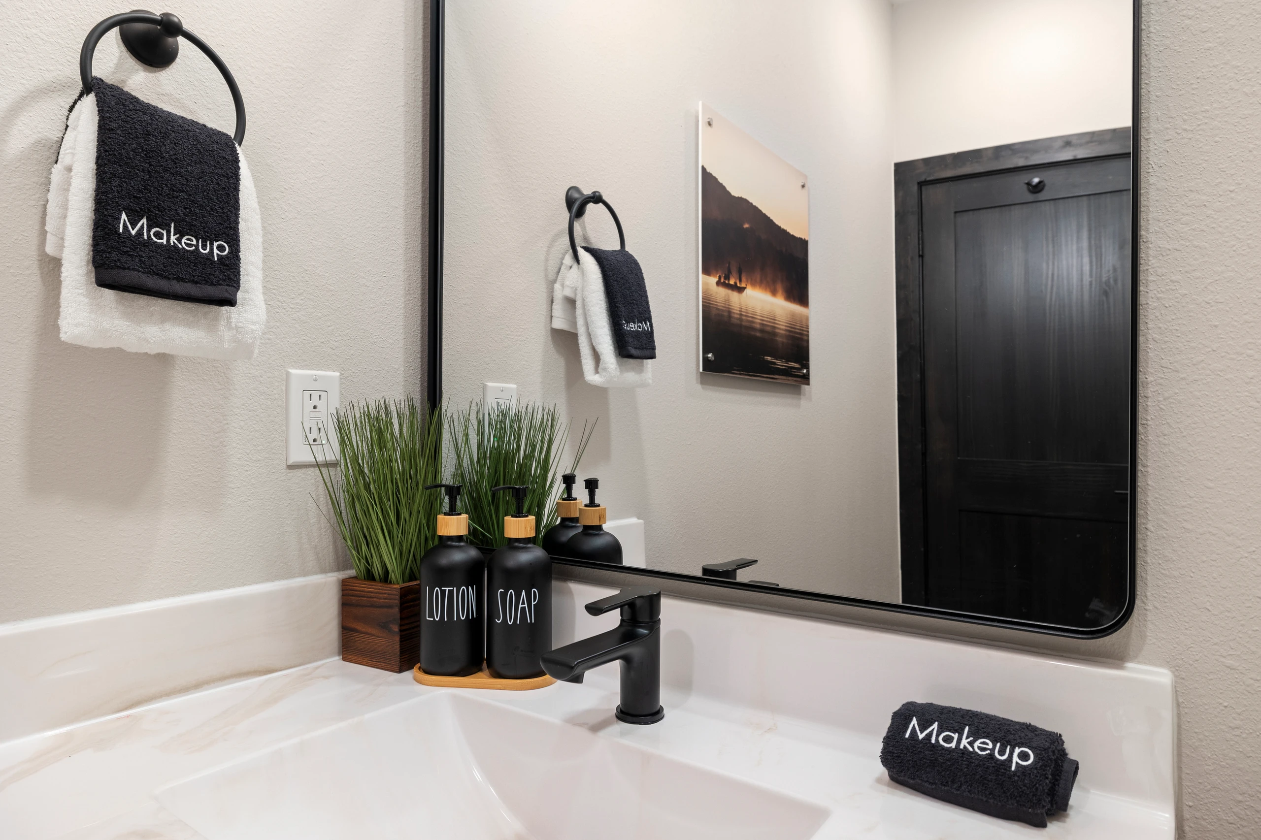 Lake-at-dawn art hangs over a black-fixture vanity.