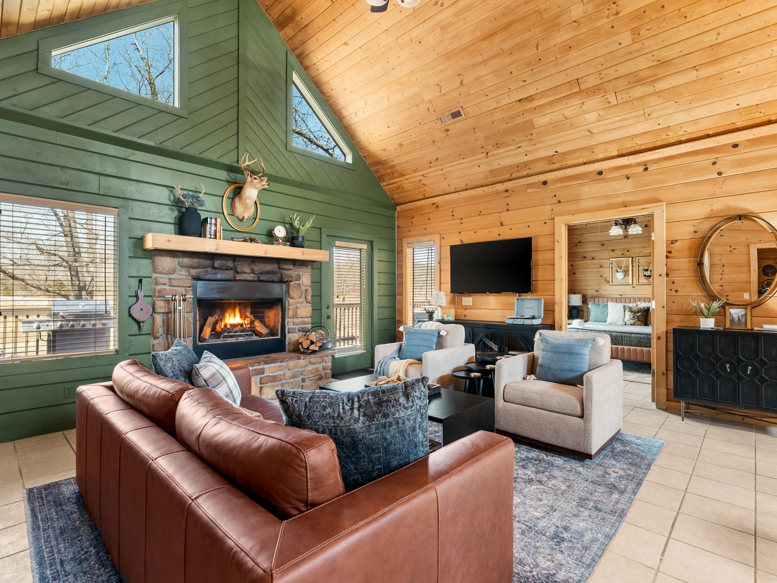 Living area with fireplace, TV and a peek into the primary bedroom. Leather sofa, comfy armchairs and room for the whole crew.