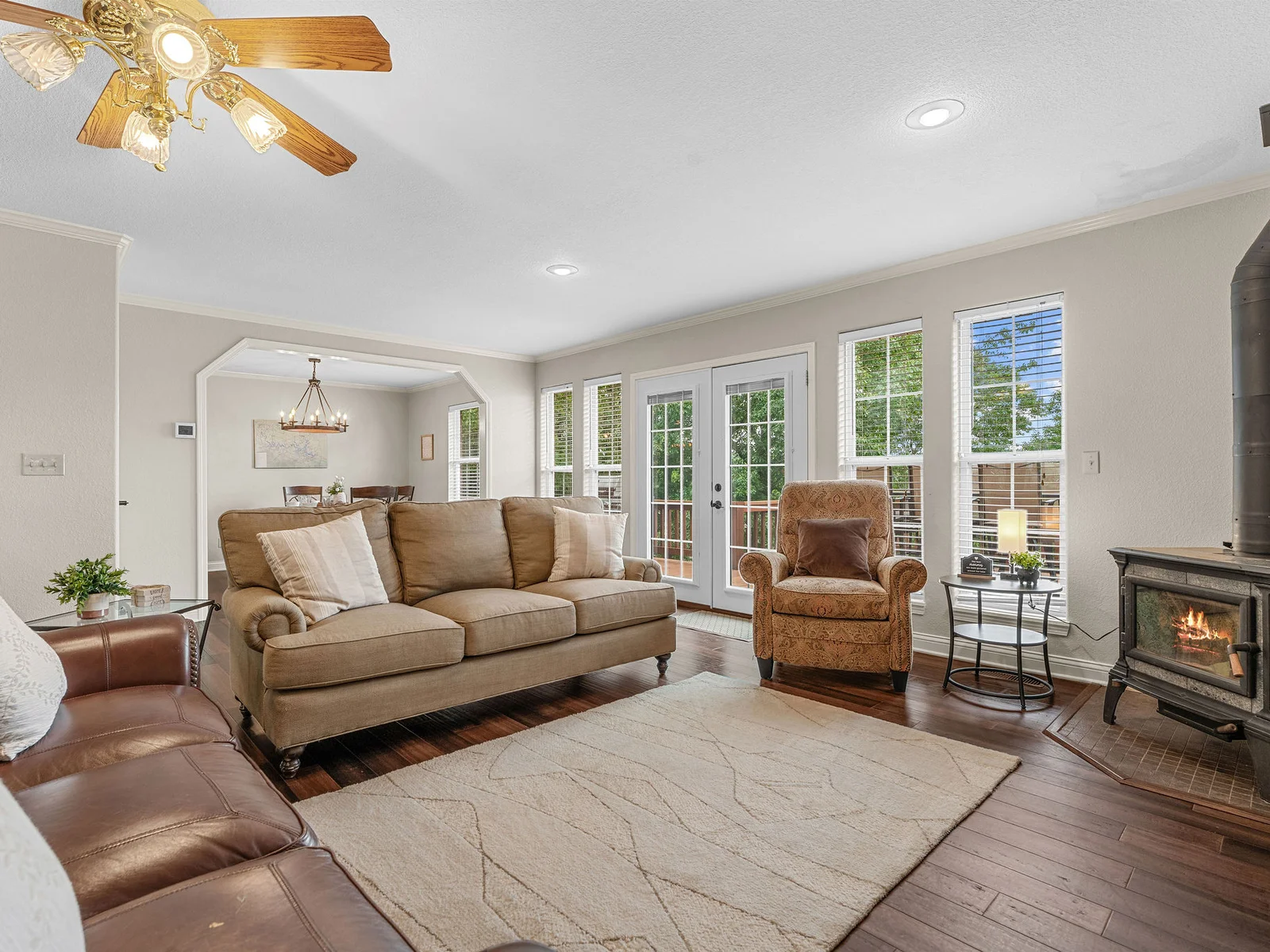 The main living room at its best — gas fireplace lit, afternoon light coming through the French doors, leather furniture arranged around the stone surround. The lake is right behind those doors.