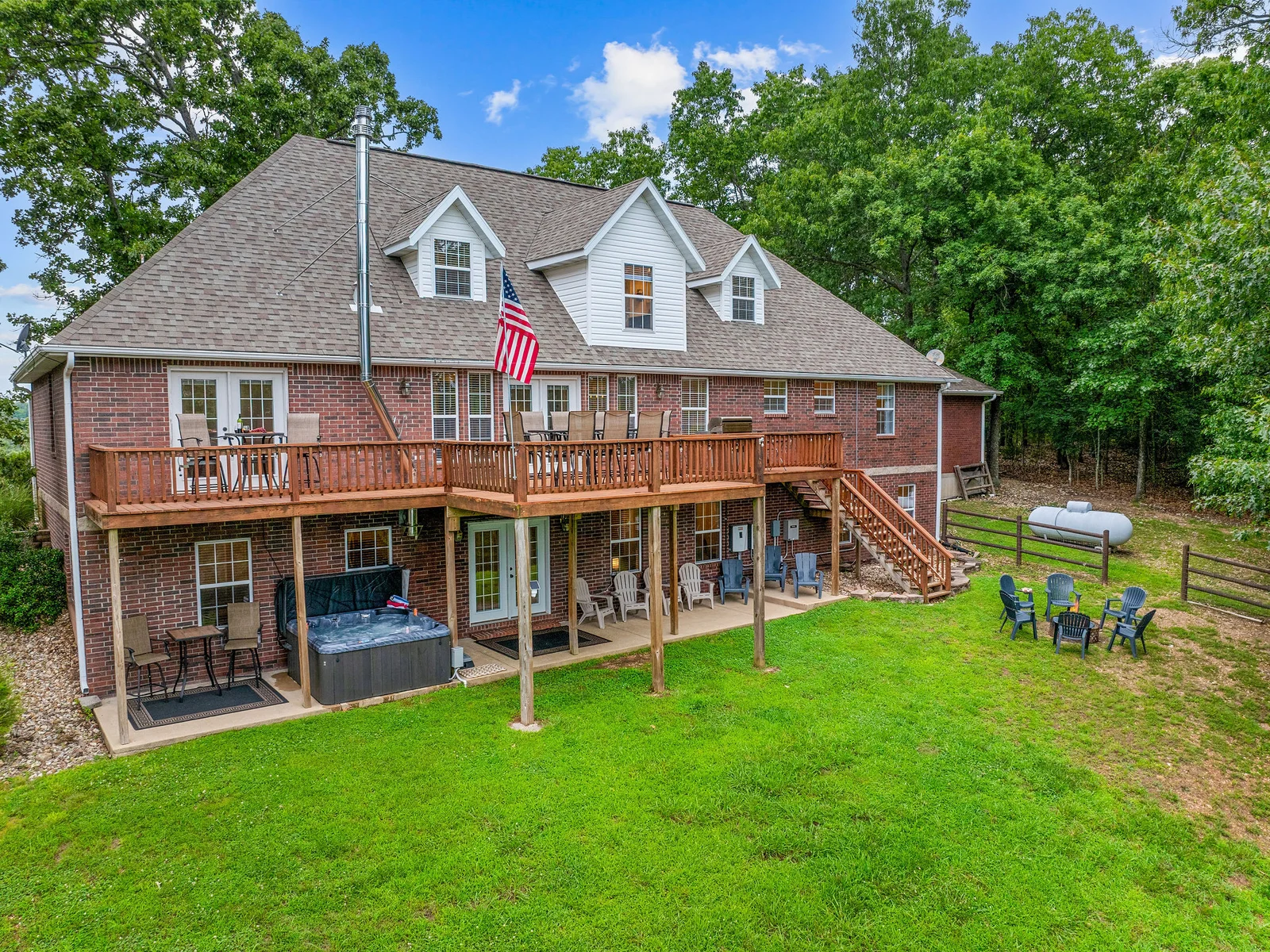 The upper deck runs the full rear of the house, stepping down to a covered lower patio with the hot tub and then out to the fire pit lawn — all of it looking straight at the lake. 179