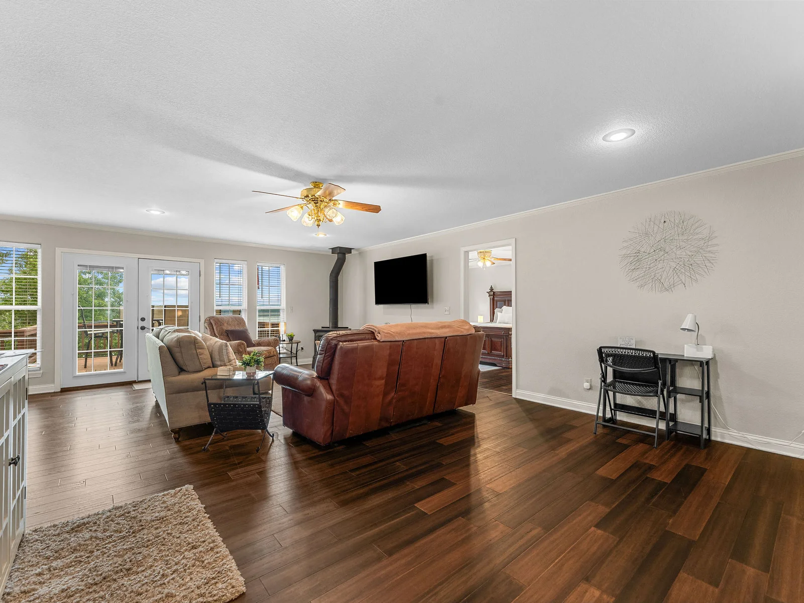 The living room opening from the entryway: dark hardwood floors, leather sofa and chairs, and French doors leading straight to the deck and the lake beyond.