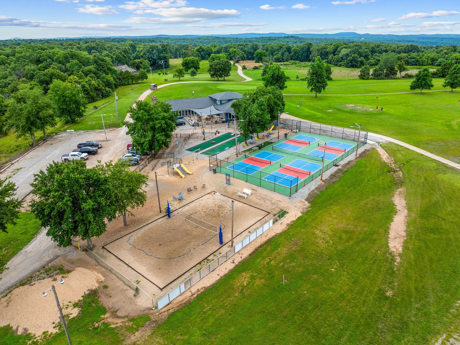 The Lost Woods Hideaway community from the air: four pickleball courts, a beach volleyball court, a clubhouse, and the lake a short walk from your front door.
