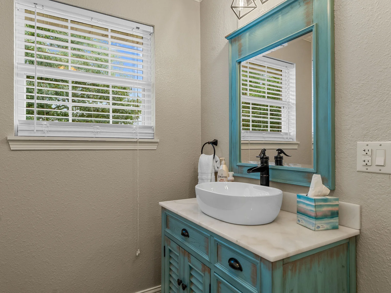 The powder room on the main floor: a vessel sink in turquoise, hand-painted tile, and a vintage-style mirror. Small but a standout — guests notice this one.
