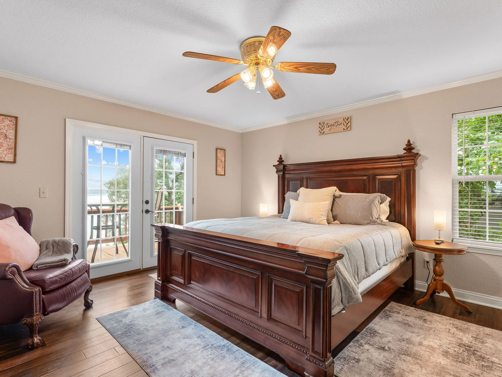 The primary bedroom: a carved king-size bed, dark walnut hardwood floors, French doors to the deck, and a direct view of Bull Shoals Lake. This is the room you book for.
