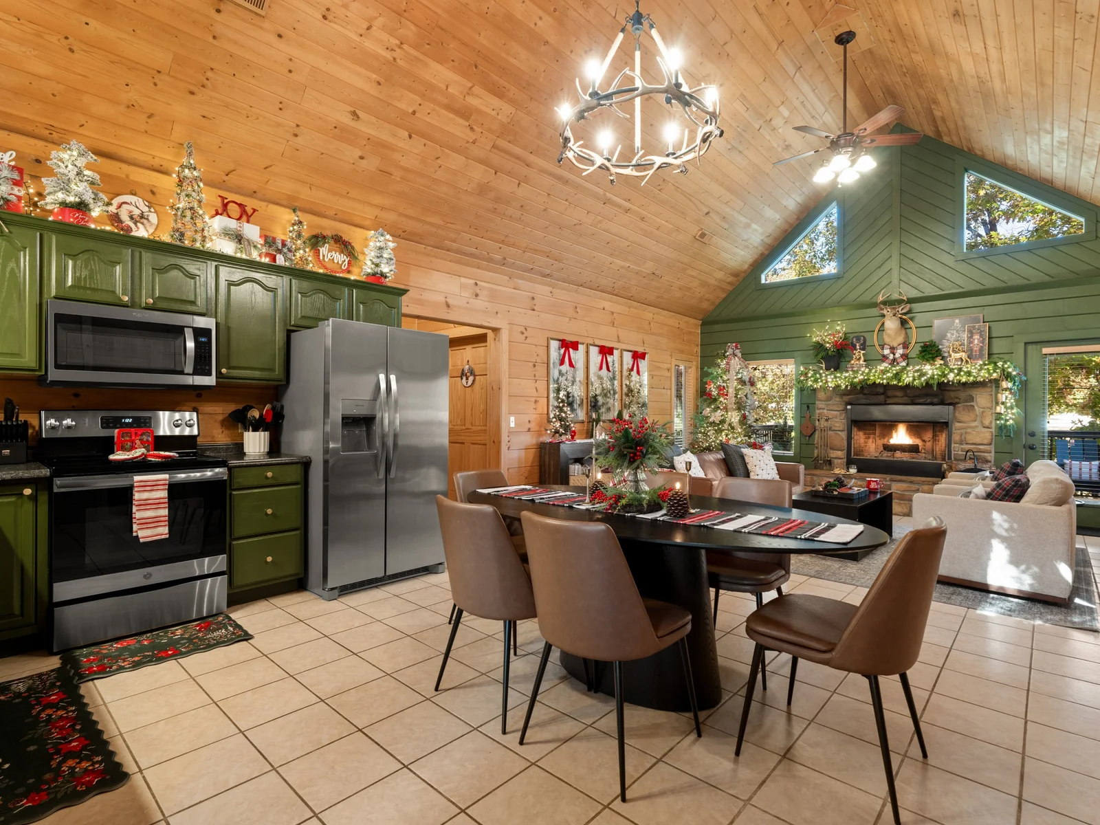 Decorated for the holidays, Nov–Jan: dining table under the antler chandelier. Garland on the cabinets, plaid runner on the table and the fire lit beyond.