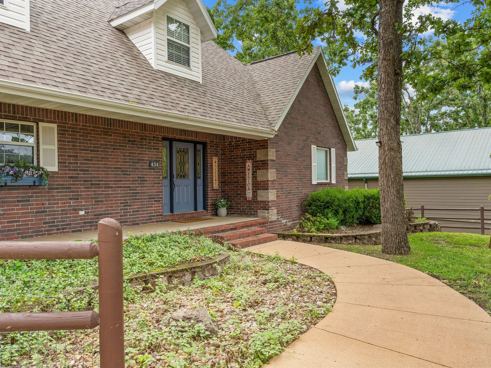 The front walkway leading to the main entry, flanked by mature trees and well-kept landscaping — your first look at the house when you arrive.