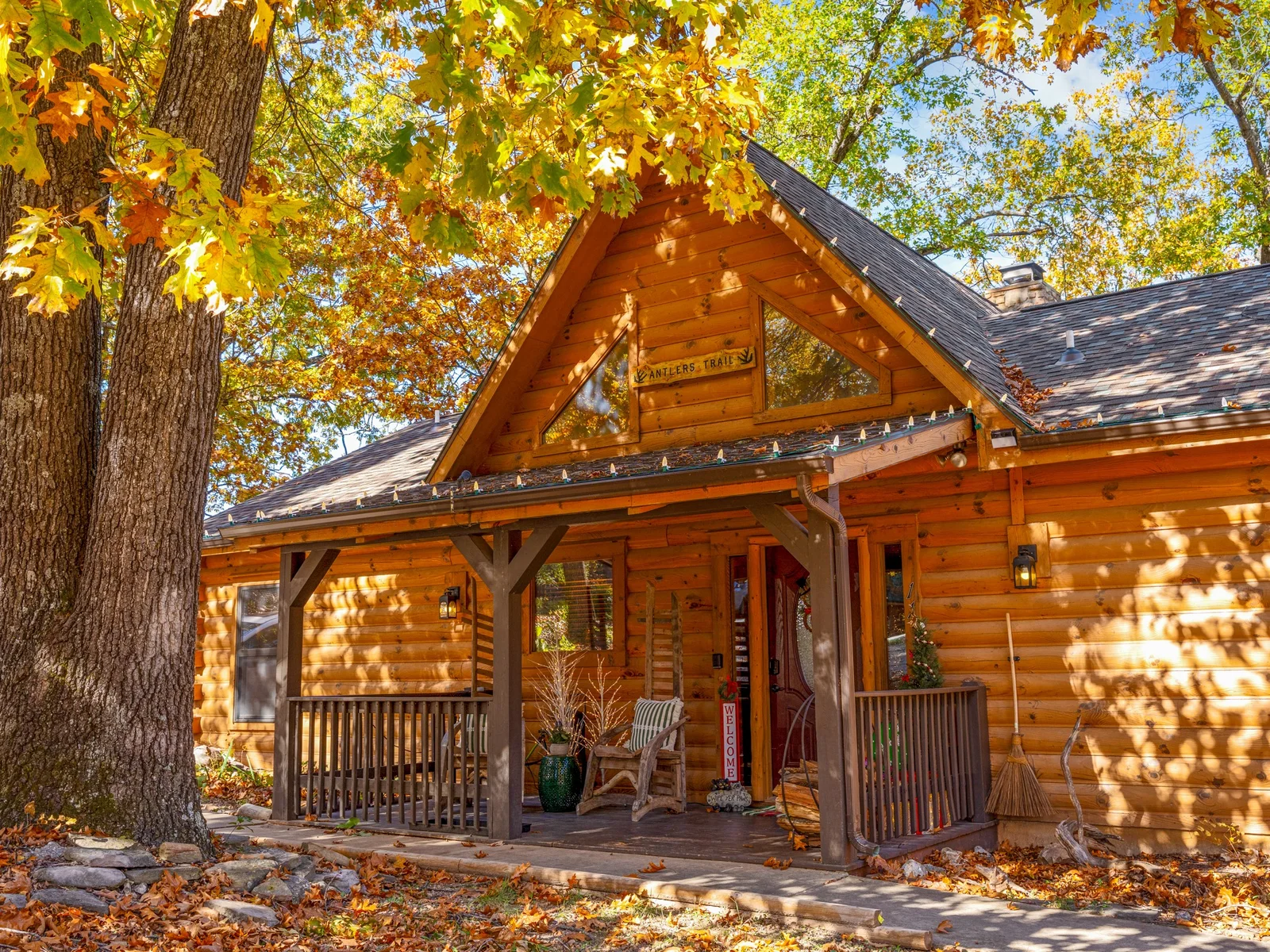 Log cabin front porch under a golden oak in fall. Grab the rocking chair and watch the leaves drift down.