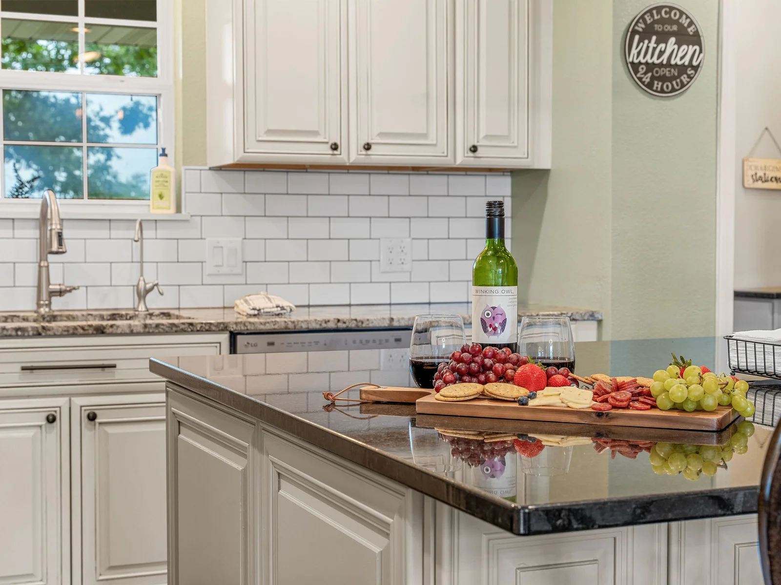 Charcuterie on dark granite, wine glasses ready, subway tile gleaming behind the island — this is what the kitchen island looks like when it is doing its best work.