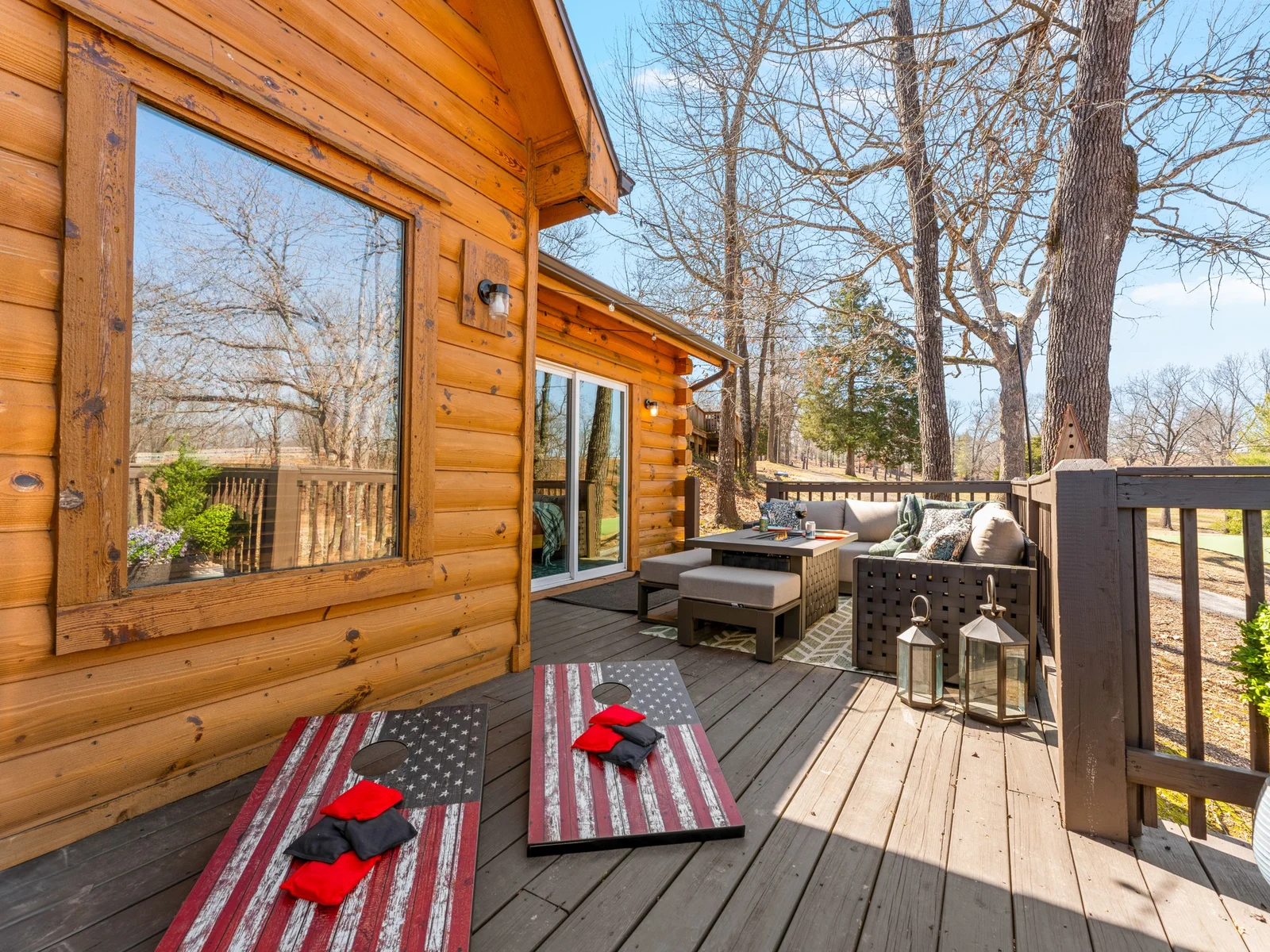 Back deck with cornhole and an outdoor sofa along the log walls. Lanterns, sunshine and a game that never really ends.