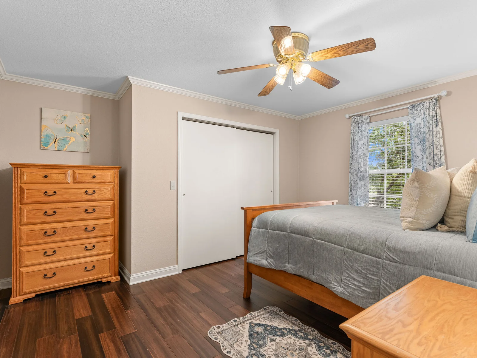 The second main-floor bedroom: queen bed with dark wood headboard, hardwood floors, and warm reading light. A quiet, clean room with direct access to the main bath.