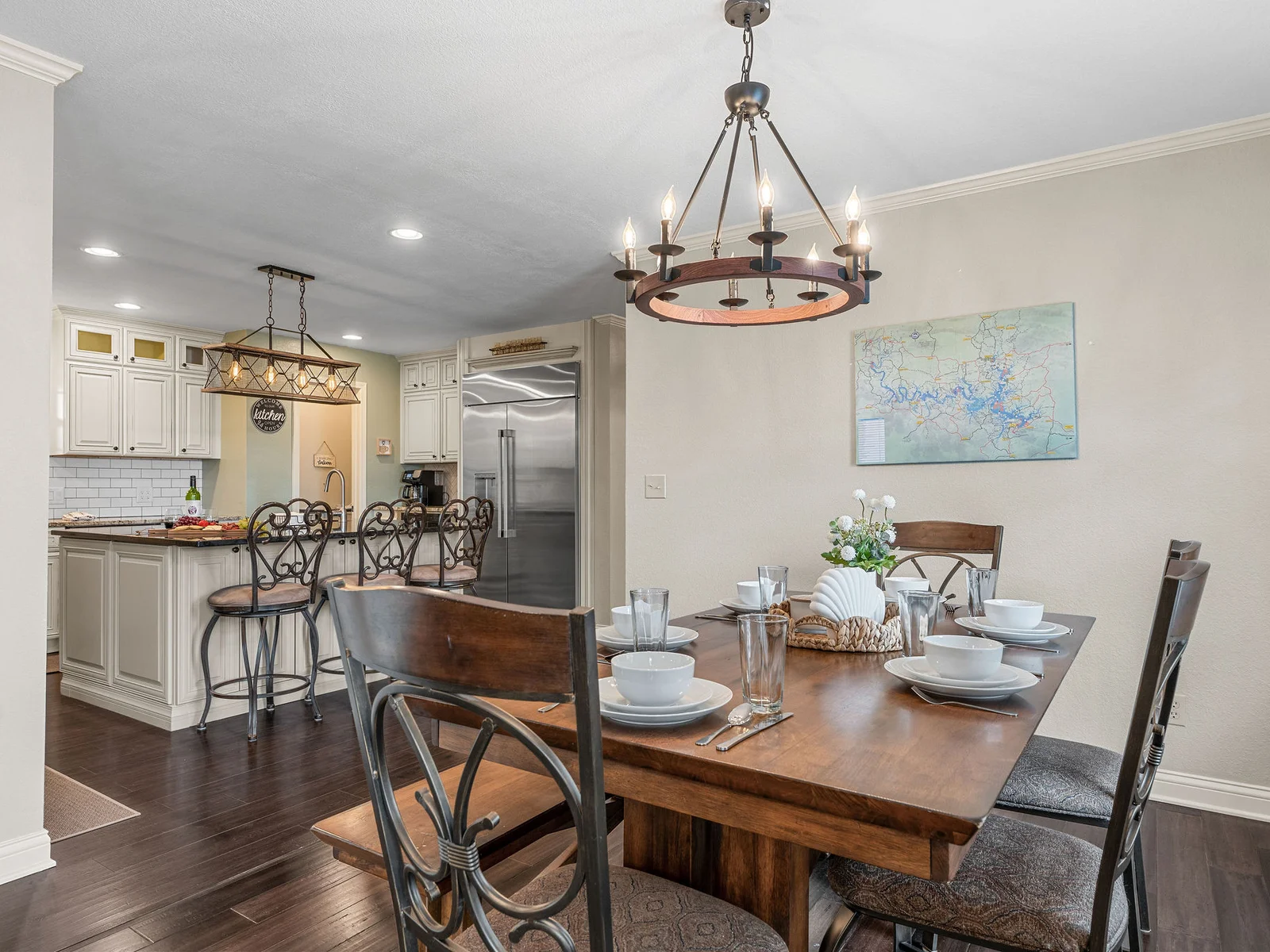 The open-plan dining room and kitchen in one frame: the chandelier-lit table, the white cabinetry, and the island behind — a proper space for gathering the whole group.