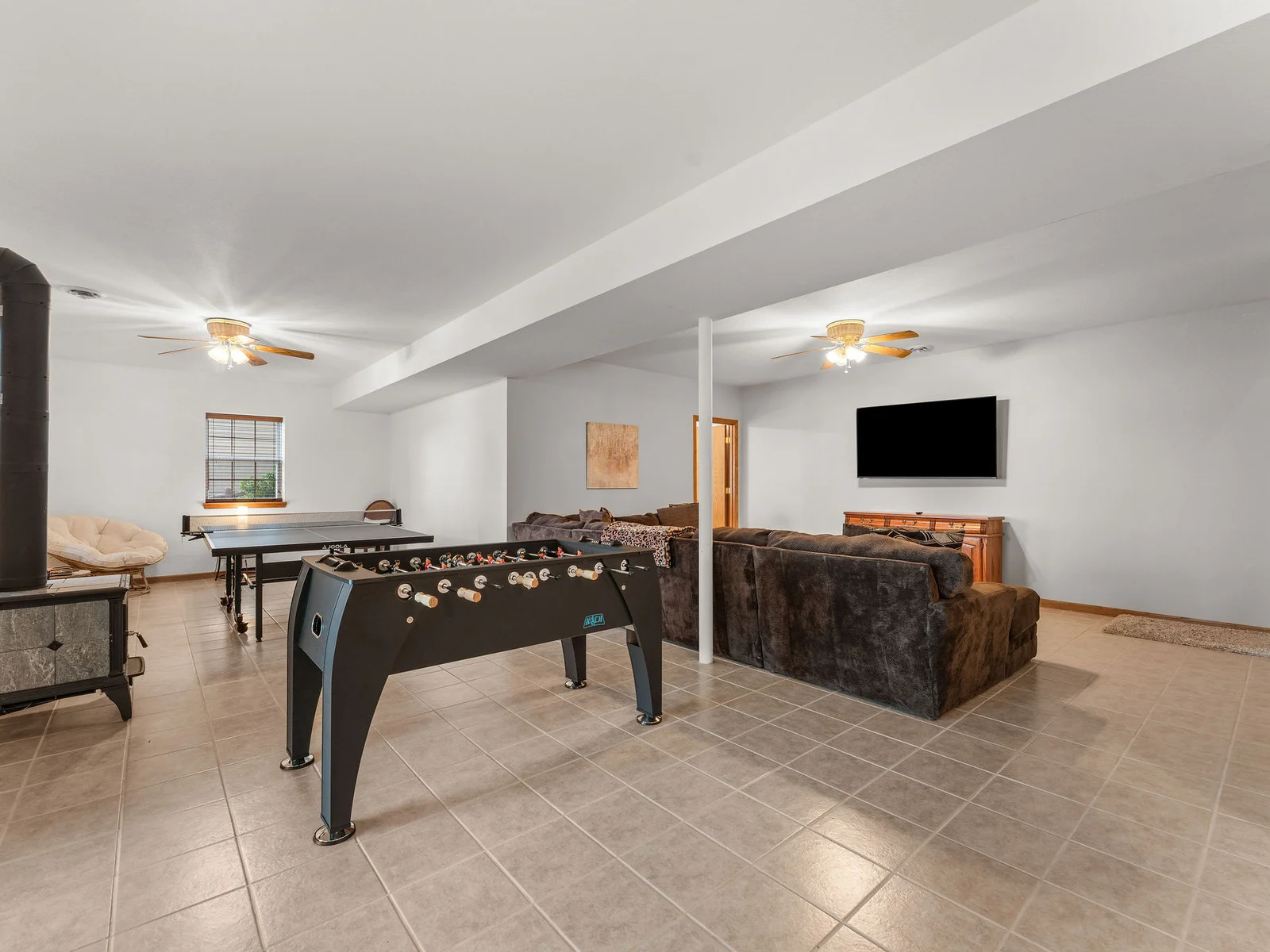 The full basement rec room from end to end: the pub table, the sectional, the foosball table, the ping pong table, and Ms. Pac-Man in the corner. A whole floor just for fun.