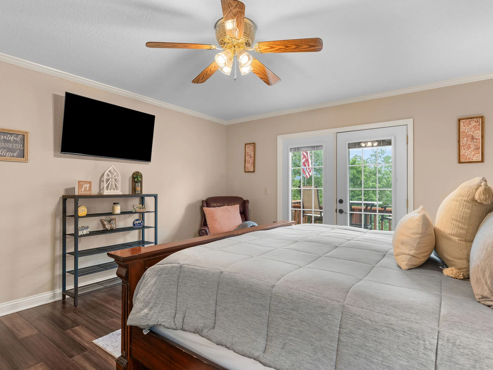 The primary bedroom from the sitting angle — TV mounted above the console, French doors open to the deck, warm light from the bedside lamps. Spacious and quiet up here.