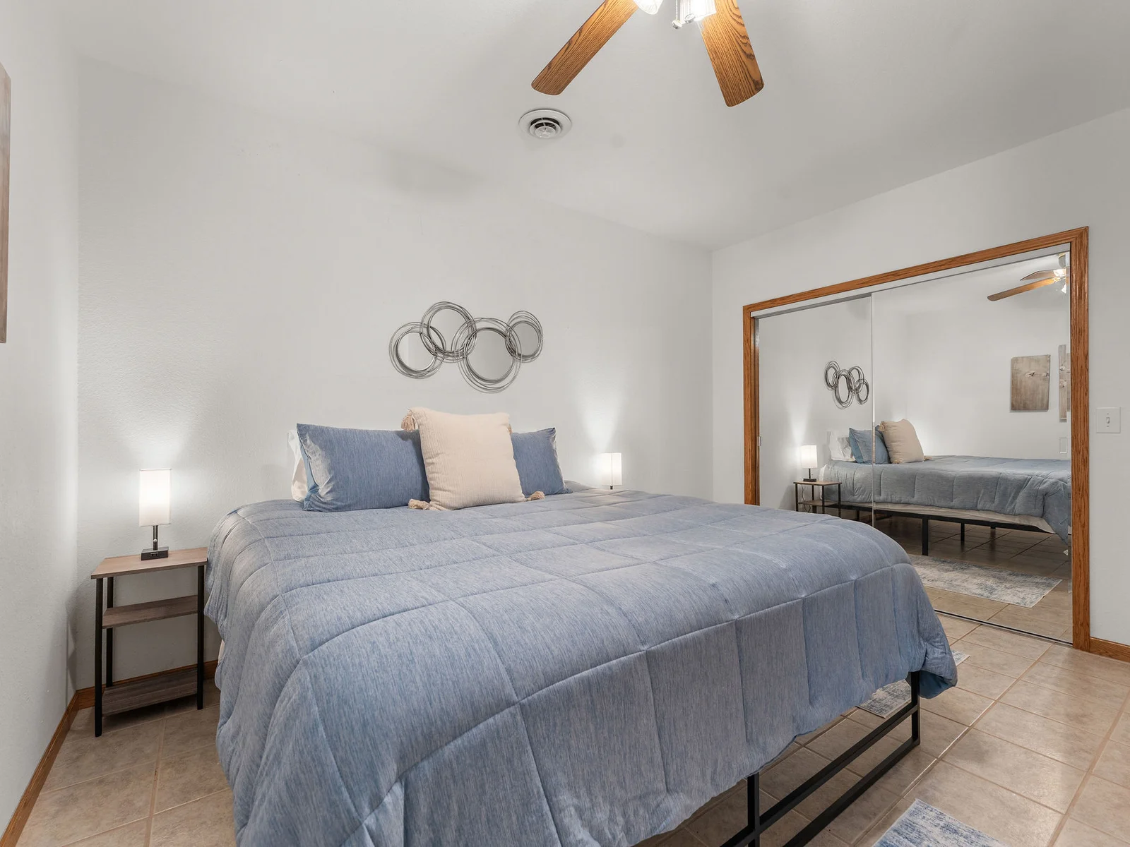 The second basement bedroom: queen bed, mirrored closet doors, and a blue-grey accent wall. Simple and comfortable — a restful room off the rec room hallway.