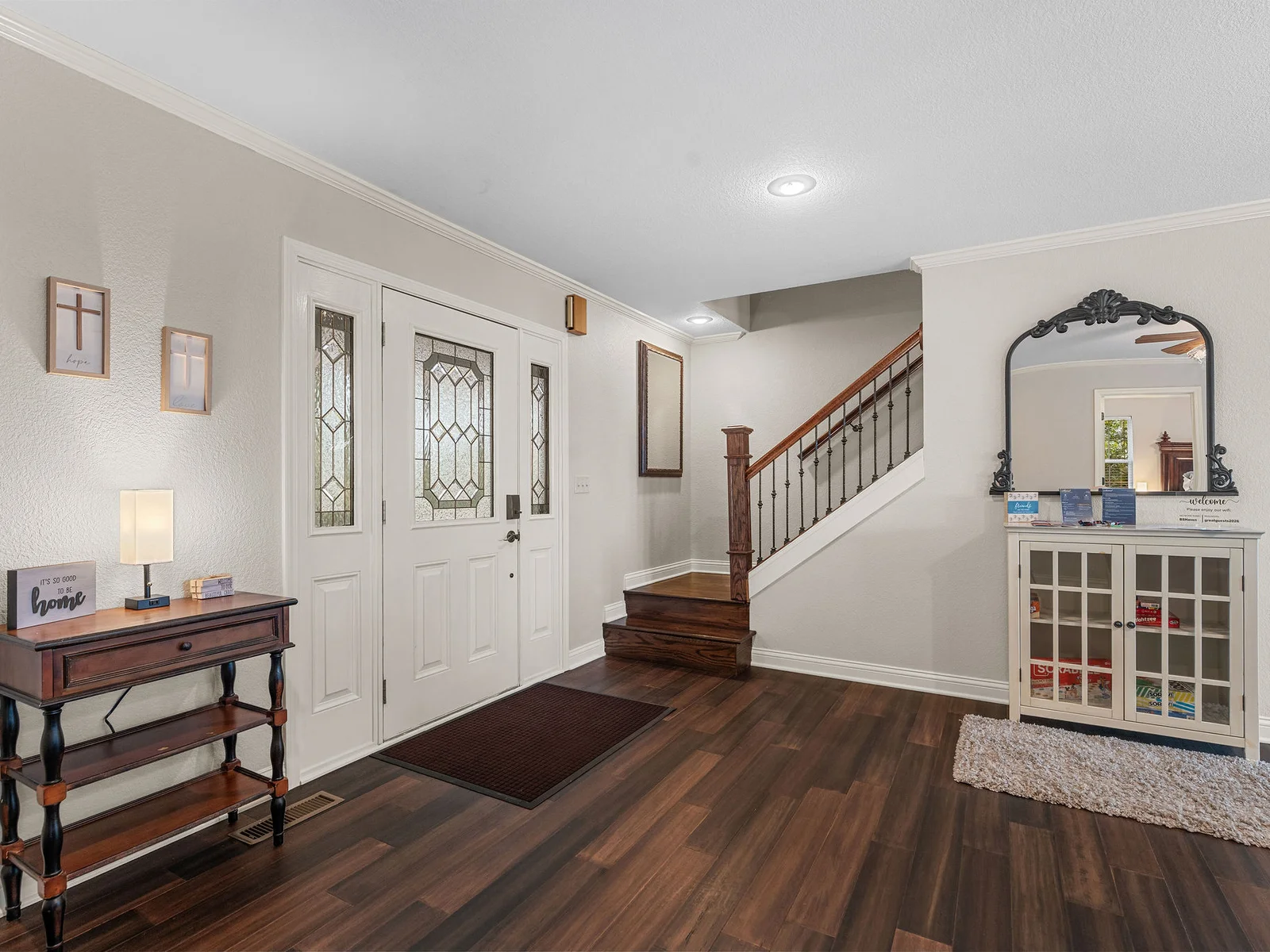 The entry foyer sets the tone: leaded glass front door, a dramatic hardwood staircase, and the lake just visible at the far end of the house. Everything opens up from here.