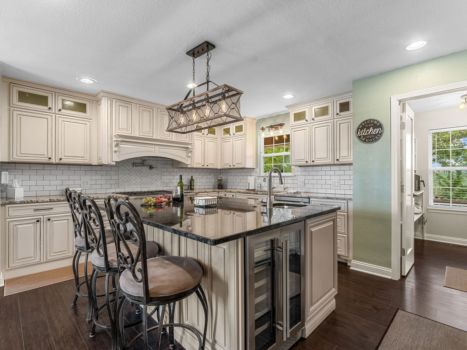 The kitchen from the island side — wine fridge, full pantry, and the herringbone backsplash that runs the whole length of the wall. Clean and fully equipped.
