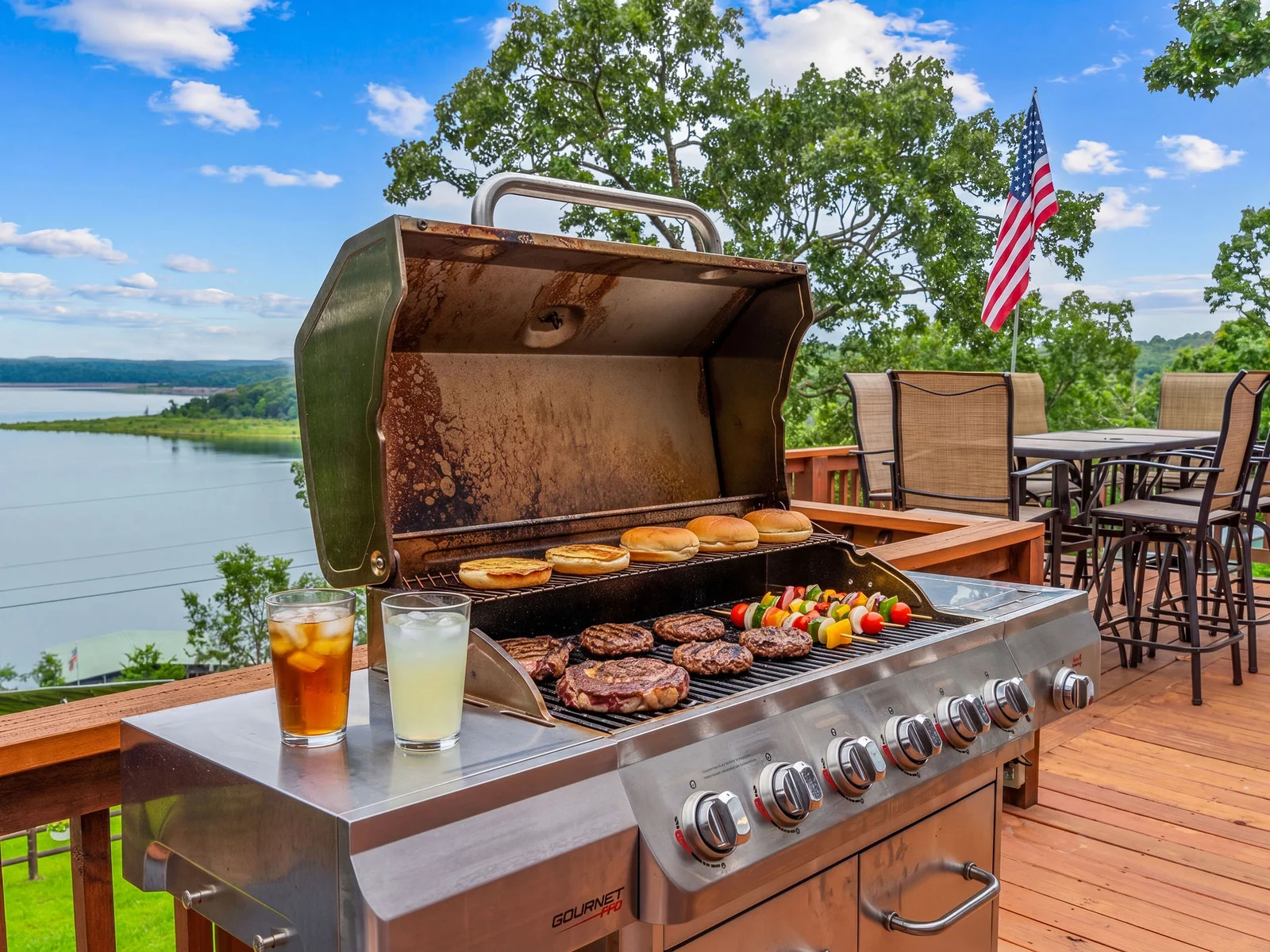 Burgers and kebabs on the grill, the lake in the background, the flag overhead — the upper deck grill station is fully set up and ready for your cookout.