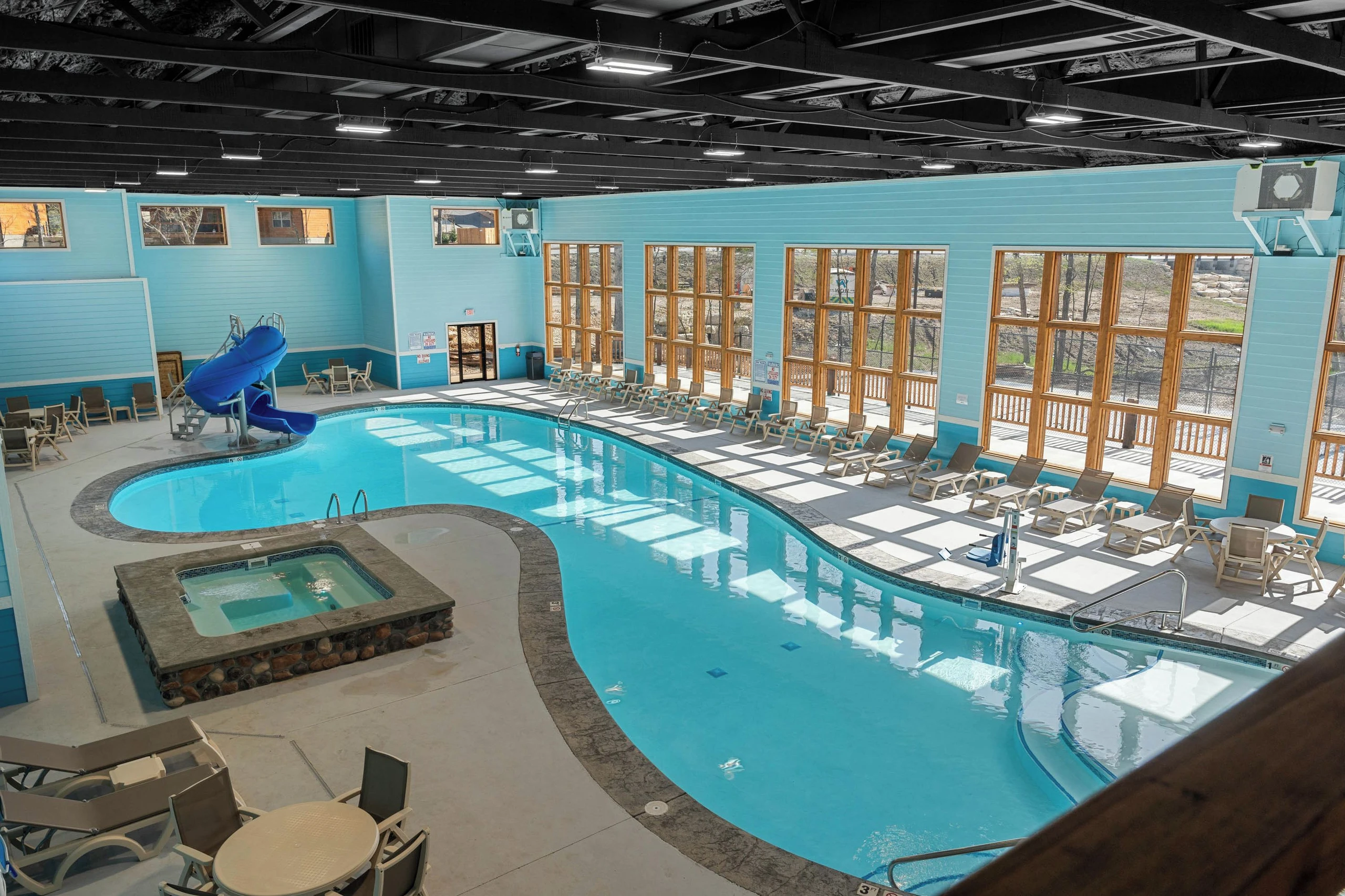 Indoor pool, cabin is visible from the windows. Wall of windows makes daytime view beautiful. Slide and hot tub in pool area.