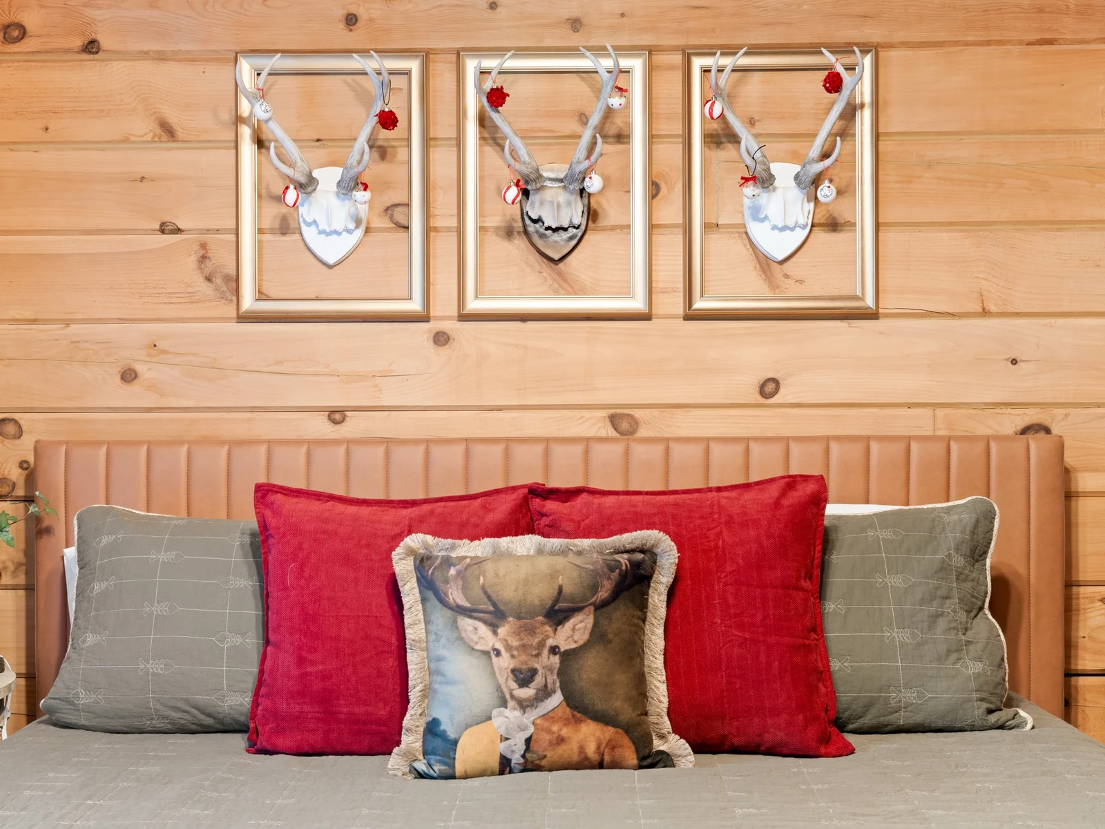 Decorated for the holidays, Nov–Jan: ornament-trimmed antlers over the bed. Red velvet pillows, a dapper deer and a leather headboard make bedtime festive.
