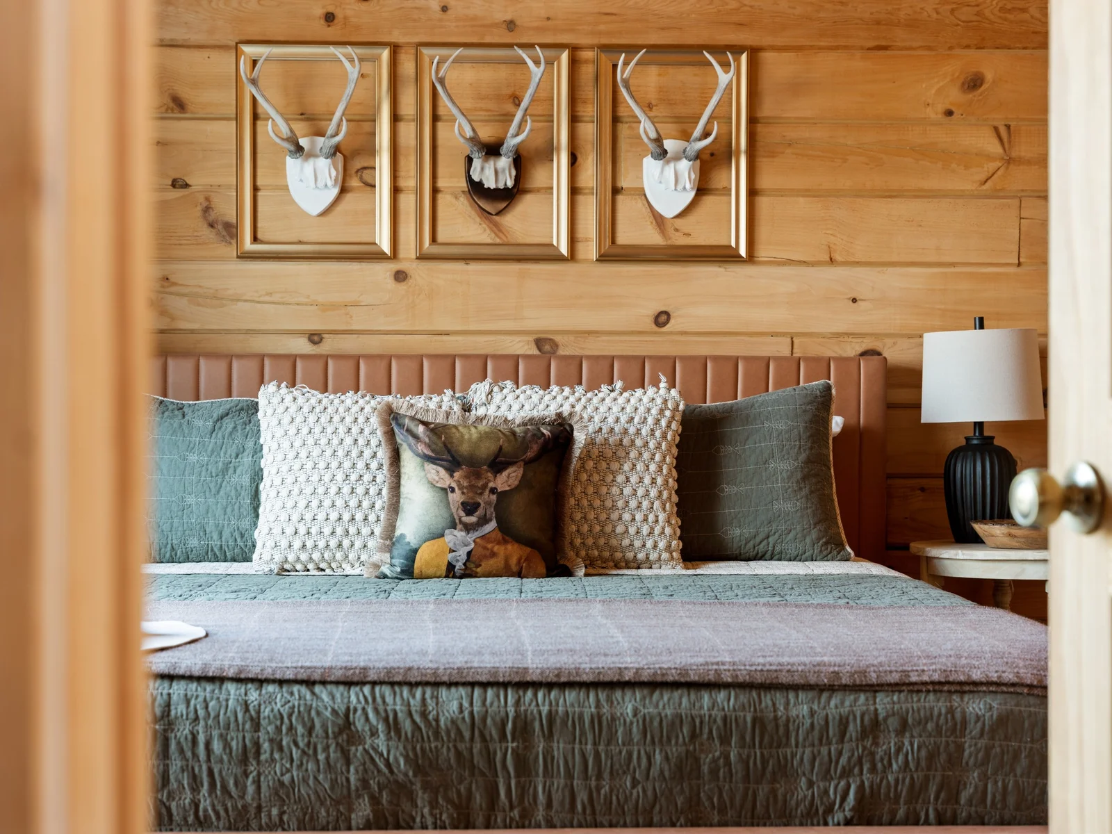 King bed in the primary bedroom with a leather headboard. Antler art above, soft pillows below and a door that closes on the world.